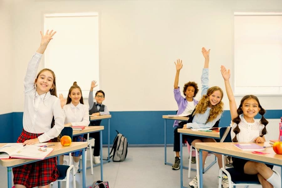 Children at their classroom desks with their hands raised