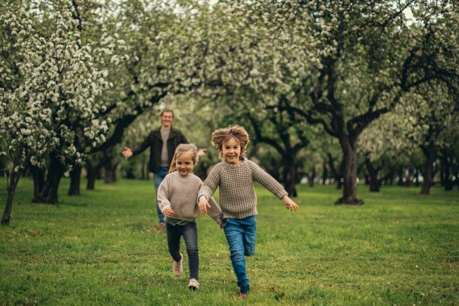 Two children running through a blossoming orchard toward a parent